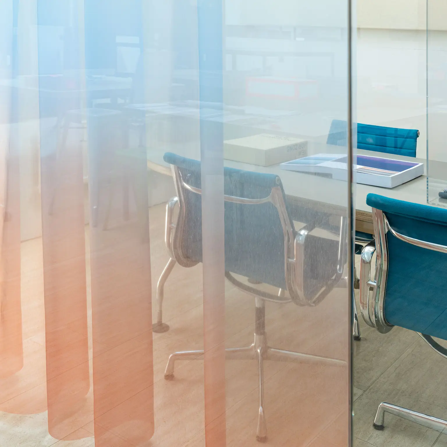 Transparent Vescom Airy curtain with a blue and orange gradient, creating a soft color wash in a modern office space.