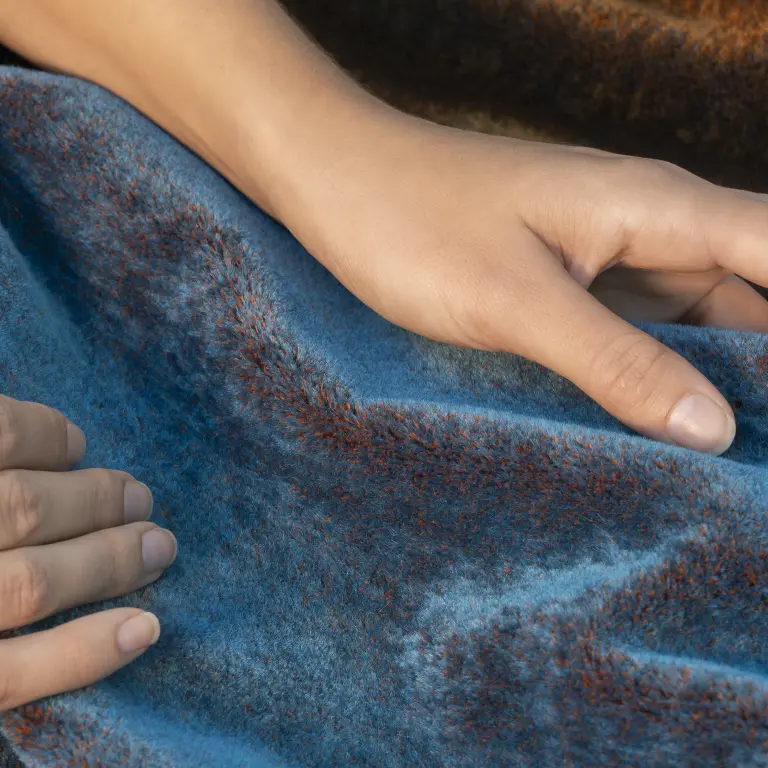 Close-up of hands touching turquoise and rust mohair upholstery fabric.