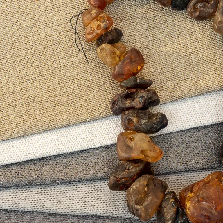 Vescom Amber woven textile wallcovering samples in different colourways with pronounced weave and amber stone necklace