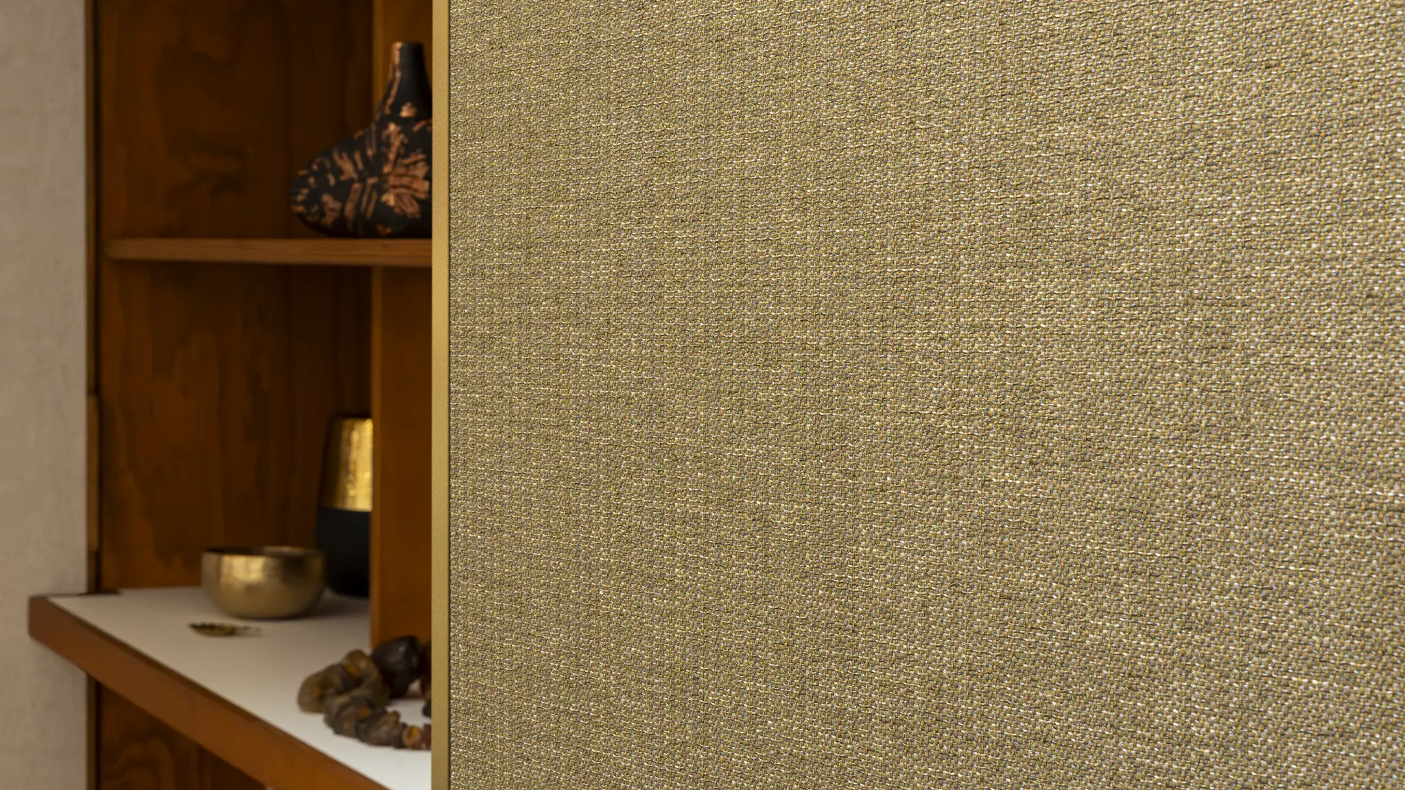 Vescom Amber woven textile wallcovering with warm gold tone and irregular melange texture beside a wooden shelving unit.
