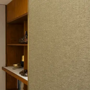 Close-up of Vescom Amber woven textile wallcovering with warm gold tone and irregular melange texture beside wooden shelving