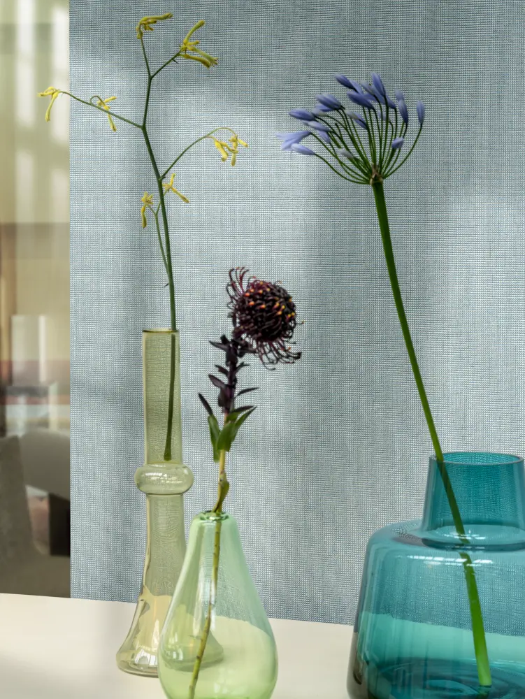 Vescom Gemstone woven textile wallcovering with small grid texture behind colourful glass vases and flowers
