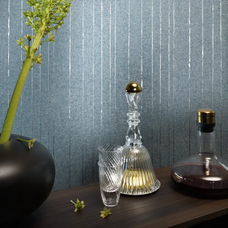 “Vescom Sofia textile wallcovering with a warm woollen weave and subtle metallic threads creating a refined shimmer, shown on interior walls behind a styled console with glass decanter, tumbler and decorative vase